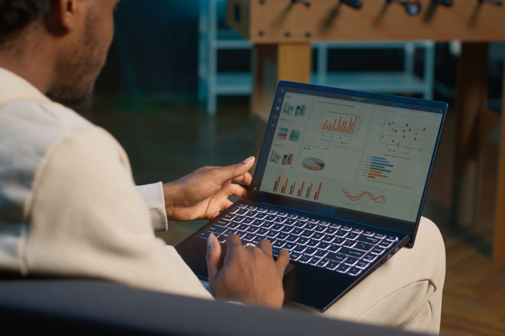 African american freelancer working from home using financial graphs, reviewing statistical data to compare supply and demand numbers. using business charts and writing on notepad. Camera A.