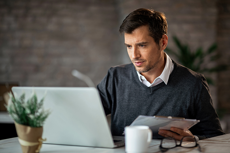 Mid adult businessman entering data from business reports in a computer at the office.
