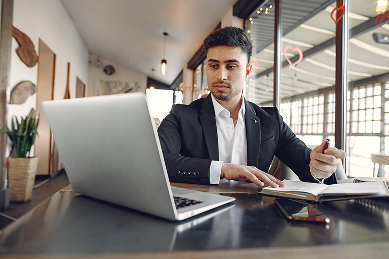 Handsome man in a black suit. Businessman working in a cafe. Guy with a laptop.
