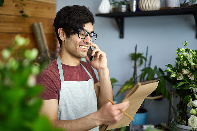 Young florist talking to client on smartphone